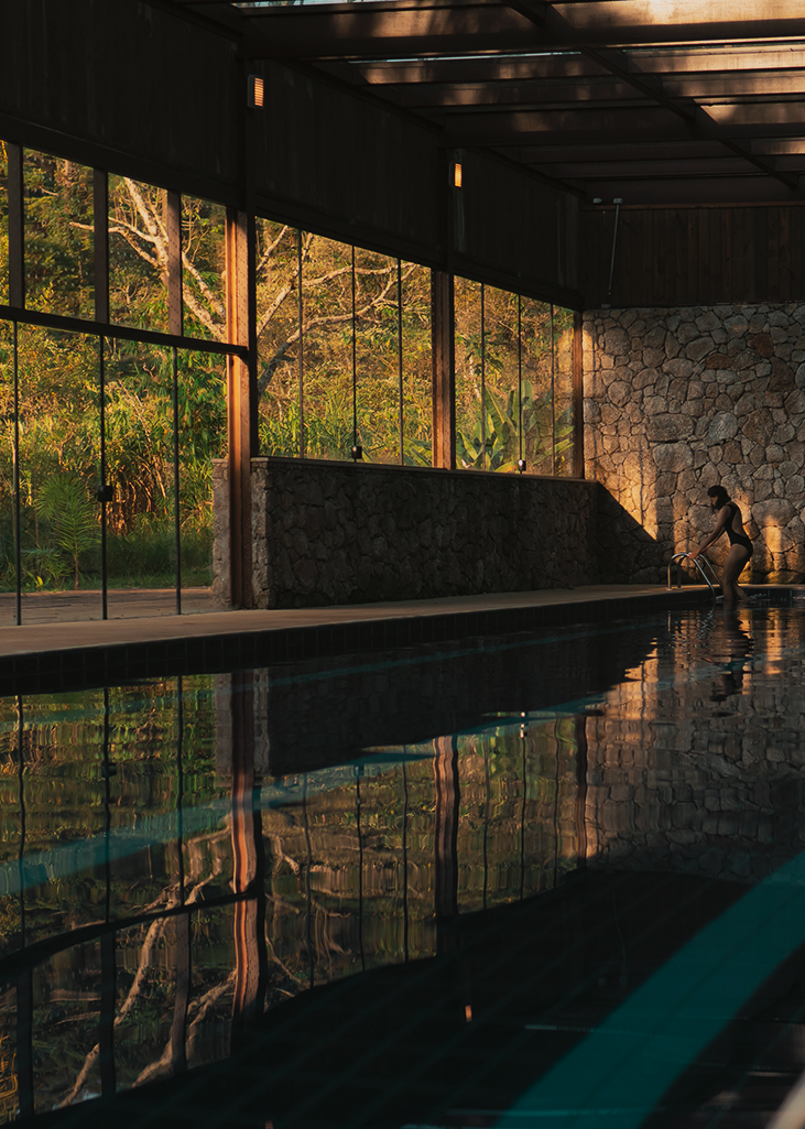 Piscina coberta com paredes de vidro e pedra ao entardecer