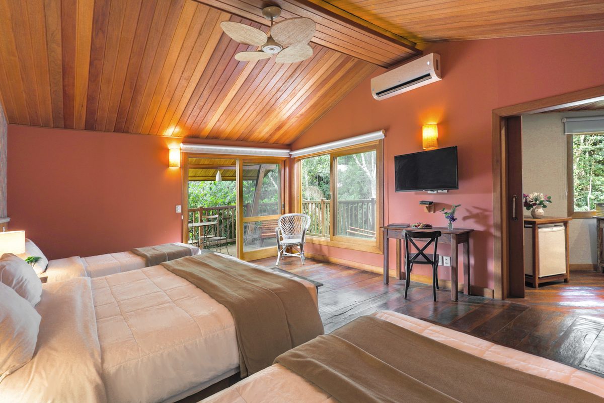Quarto do Bangalô Master com camas, mesa de trabalho e varanda para a mata